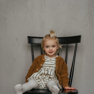 Bébé fille en robe et gilet sur une chaise noire